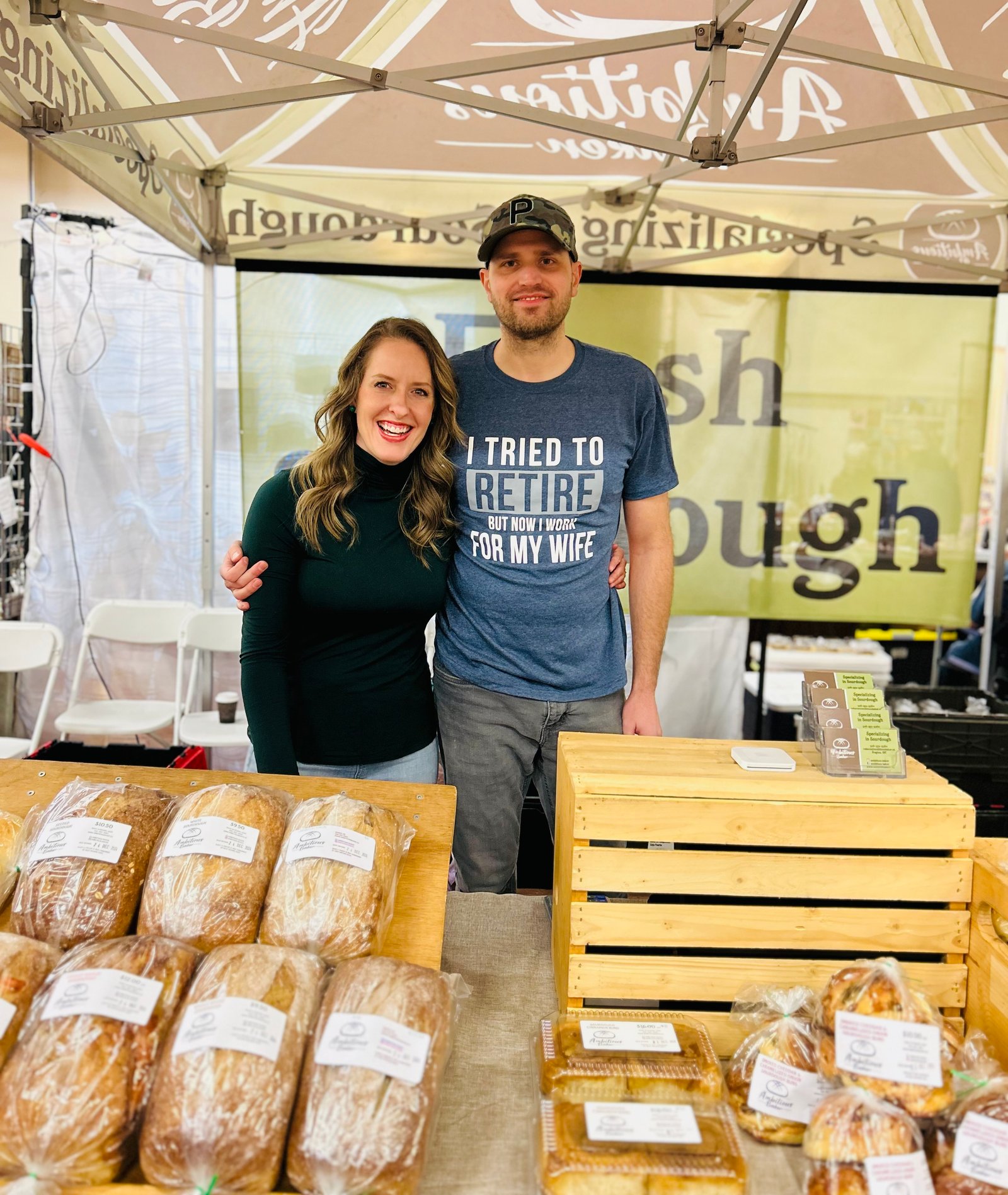 Ambitious Baker owners Quinn and Rebecca standing together behind their sourdough market stall in Regina, Saskatchewan