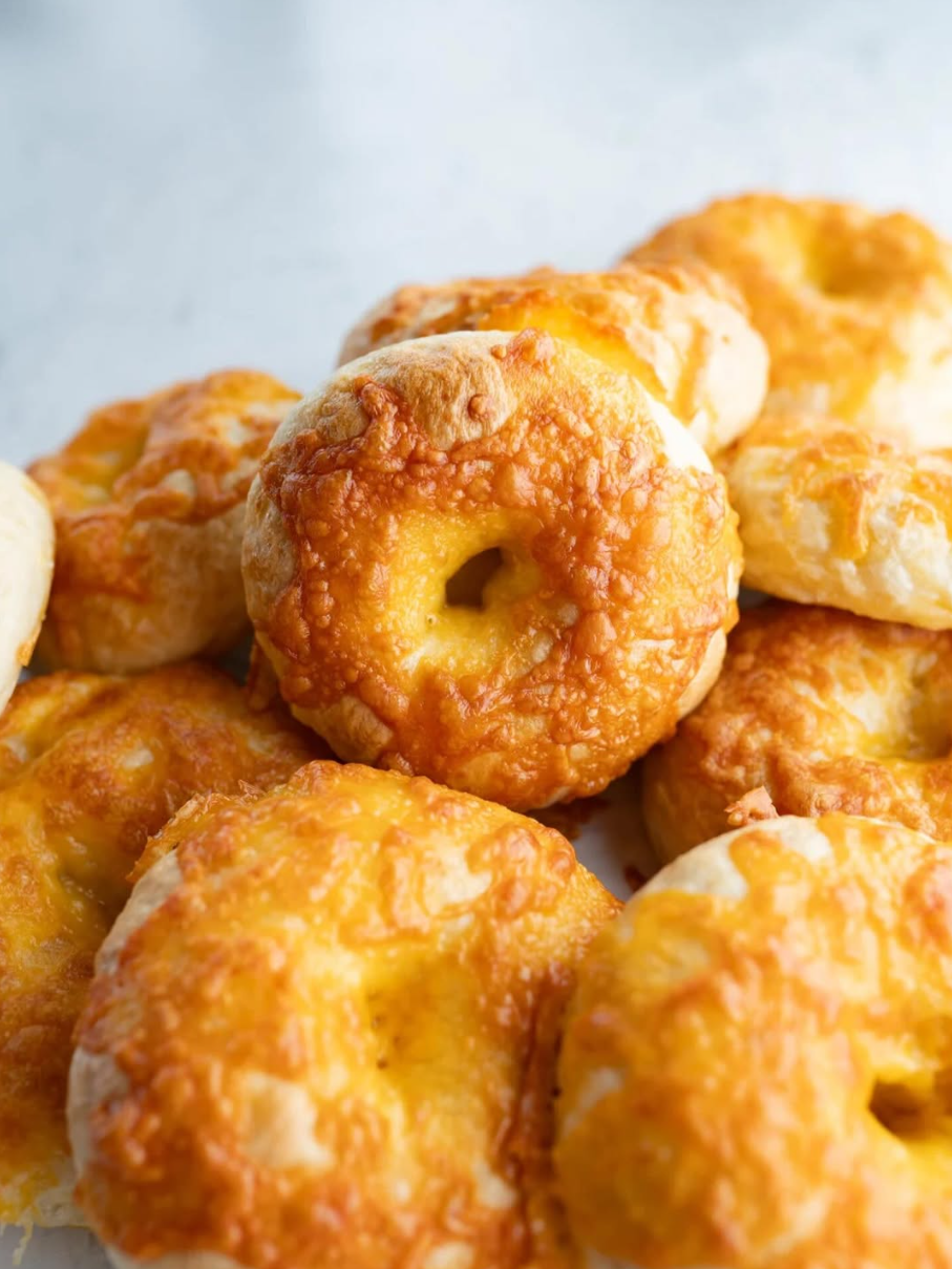 A stack of cheddar sourdough bagels topped with crisp, golden melted cheese