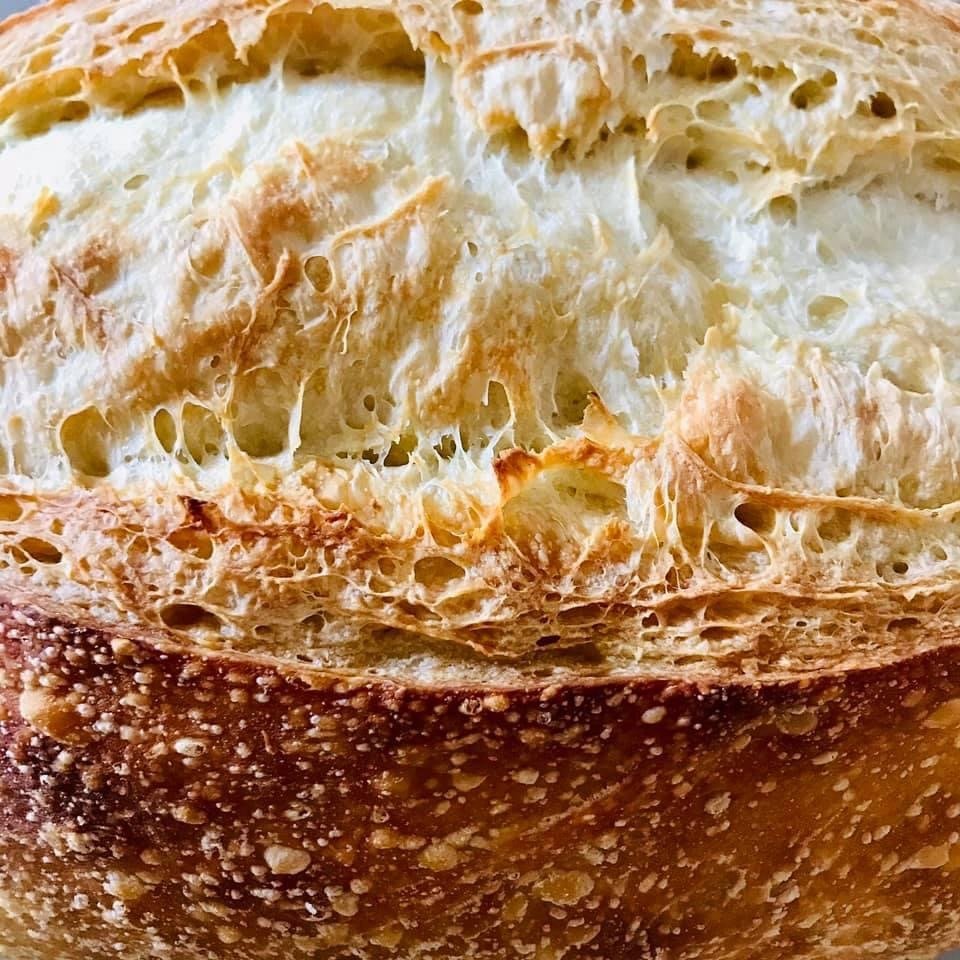 A baker’s hand scoring a floured sourdough loaf with a blade