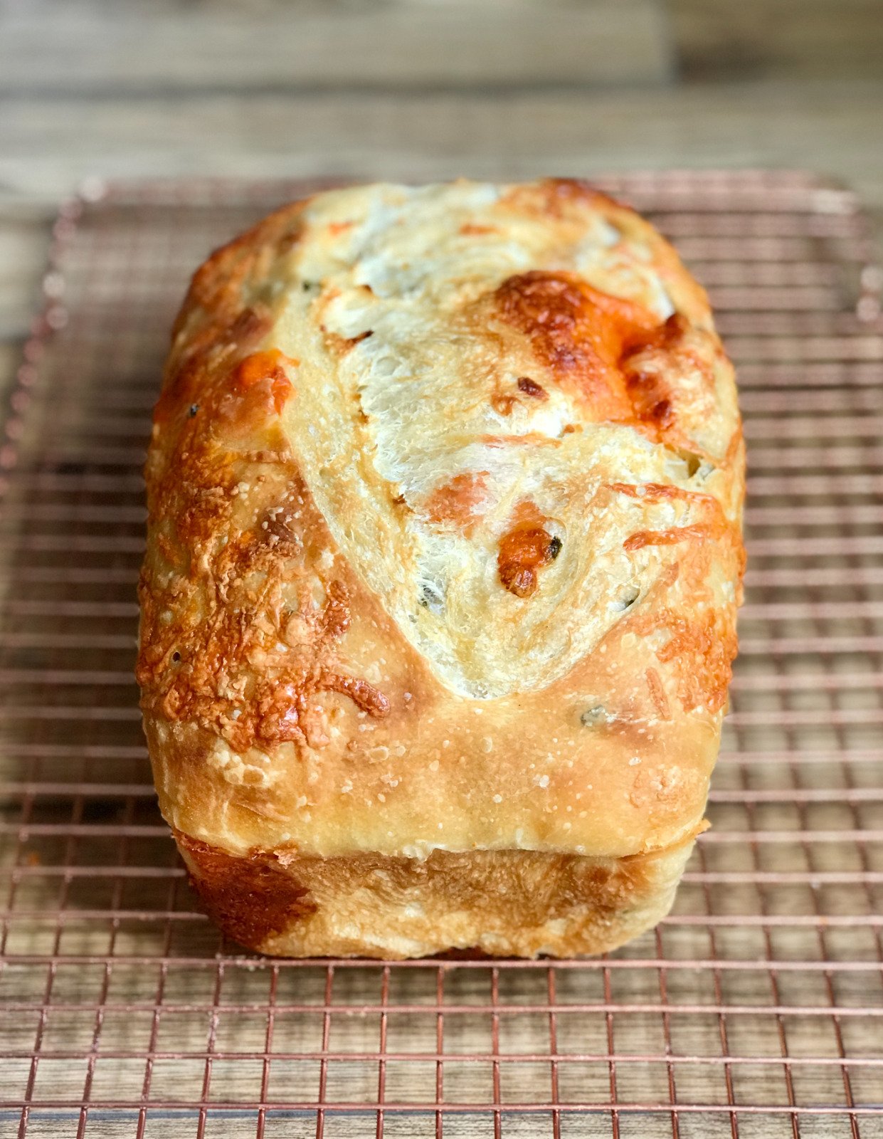 A jalapeño cheddar sourdough loaf with melted cheese and pepper flecks across a golden crust