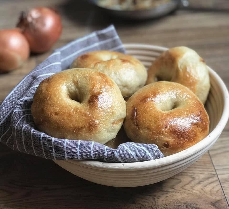 Four plain white sourdough bagels nestled in a linen-lined proofing basket